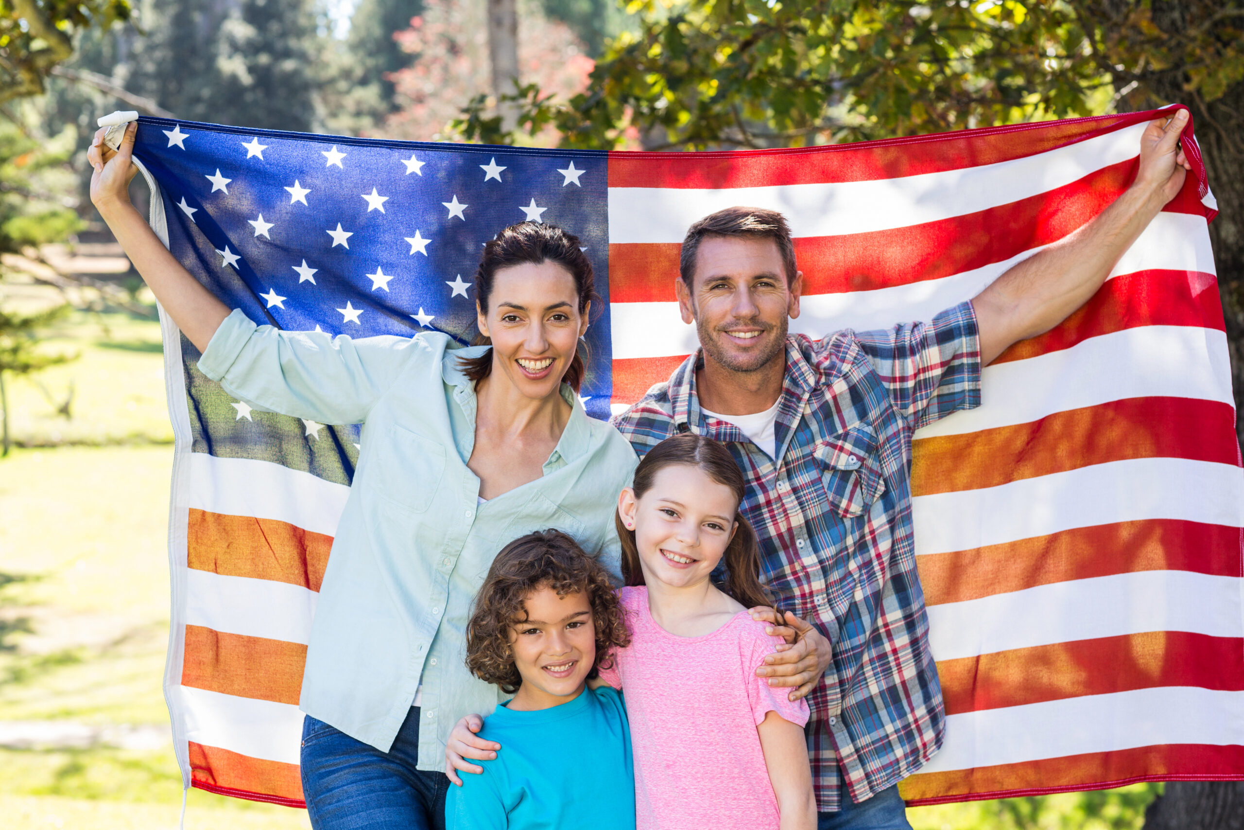 Happy family smiling with an american flag in a park on a sunny day
