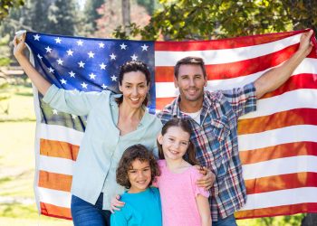 Happy family smiling with an american flag in a park on a sunny day